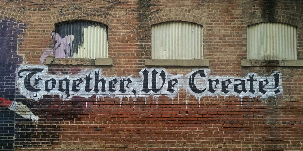 "Togerher. We Create!" on a brick wall.