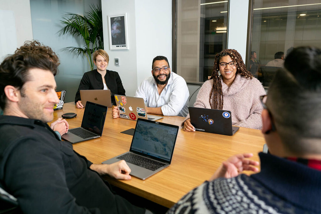 [Alt-teksti: A group of persons sitting at the table with their laptops.]