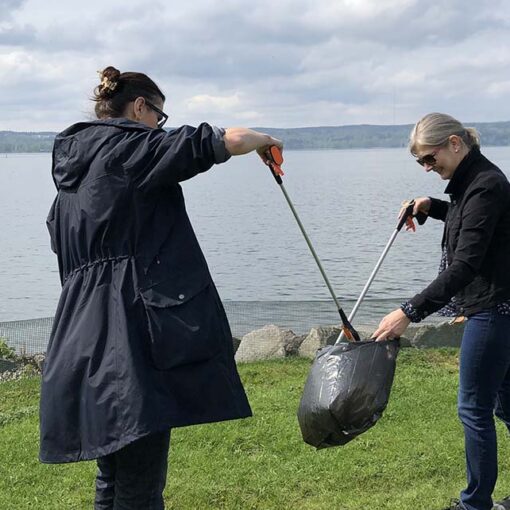 Three people by the lake collecting and picking up trash with litter picking sticks.