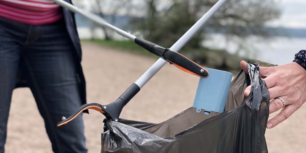 Trash bag and two litter picking sticks, putting plastic debris in the trash bag.