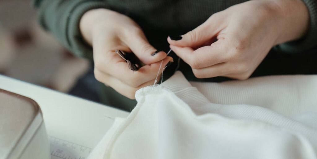Two white hands with black nail polish, mending a white sweater.