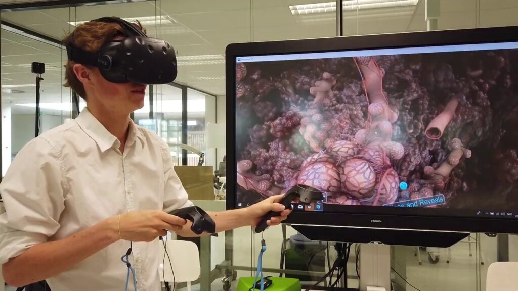 [Texto alternativo: un joven entrenando con gafas de realidad virtual y manijas frente a una pantalla que muestra una imagen detallada de los órganos humanos.]