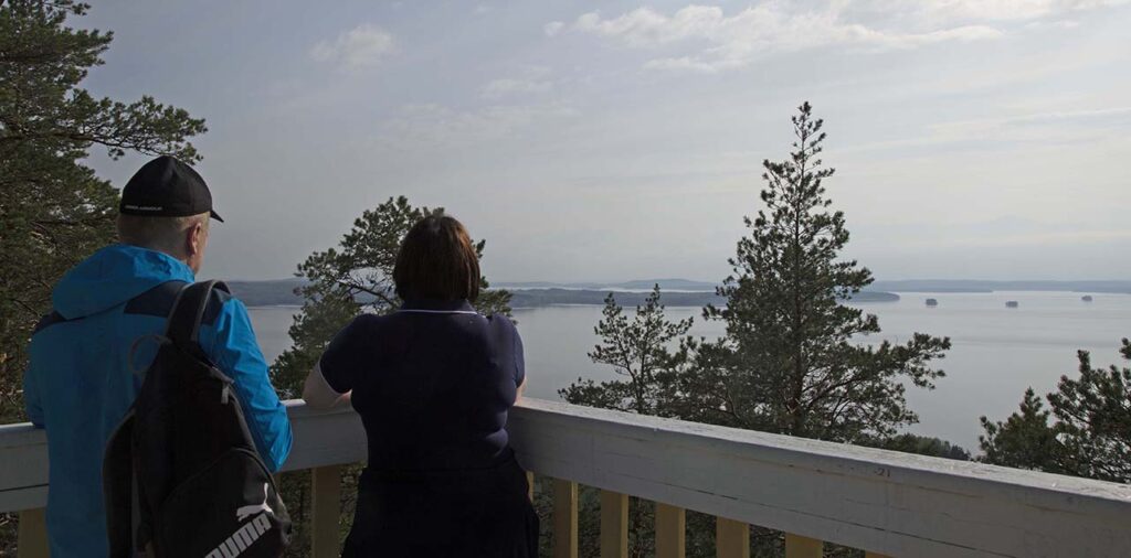 [Alt-teksti: Näkötornin ylätasanteella kaksi henkilöä katselee järvelle avautuvaa maisemaa havupuiden latvojen lomasta.]