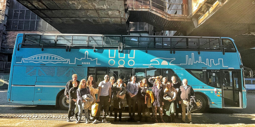 A photo of a group of people standing in front of a blue duple-decker bus, which has a logo of Ostrava painted on the side. 