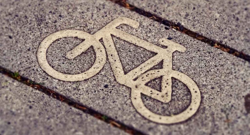 [Alt-teksti: lähikuva katukiveyksestä, jossa on pyörän kuvasymboli pyörätien merkkinä.]