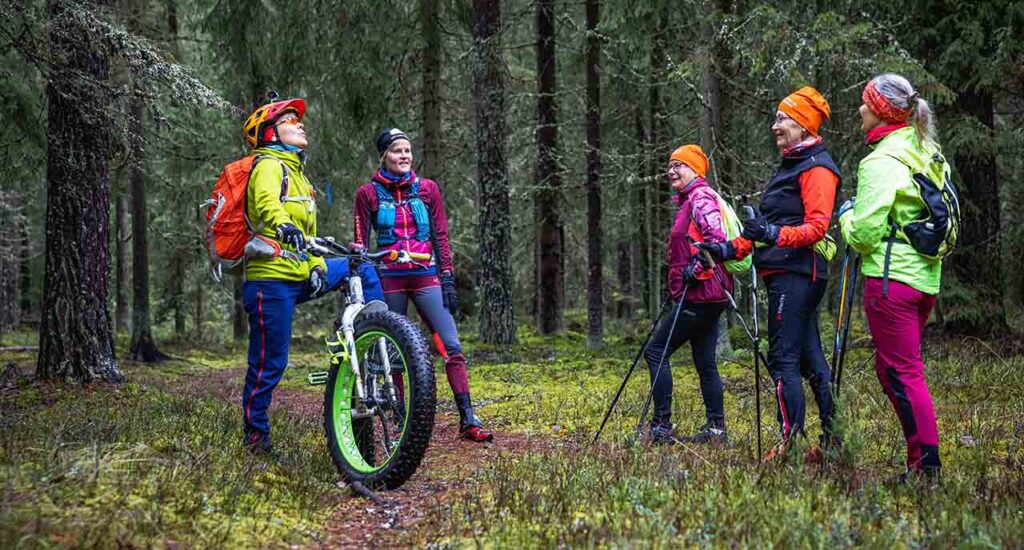 [Alt-text: A group of persons in a forest, with equipment of nordic walking and bicycling.]