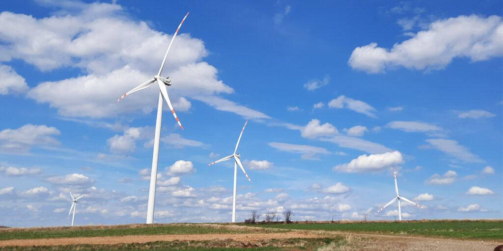 A photo of five wind turbines. It is a sunny day with some white clouds in the sky.
