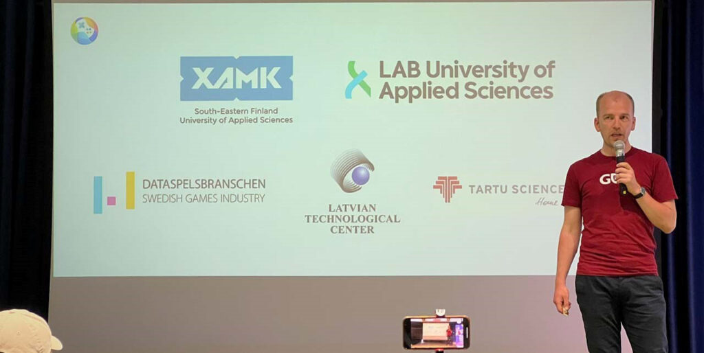 [Picture of a man on the stage. Behind him a slide with logos of different project partners]