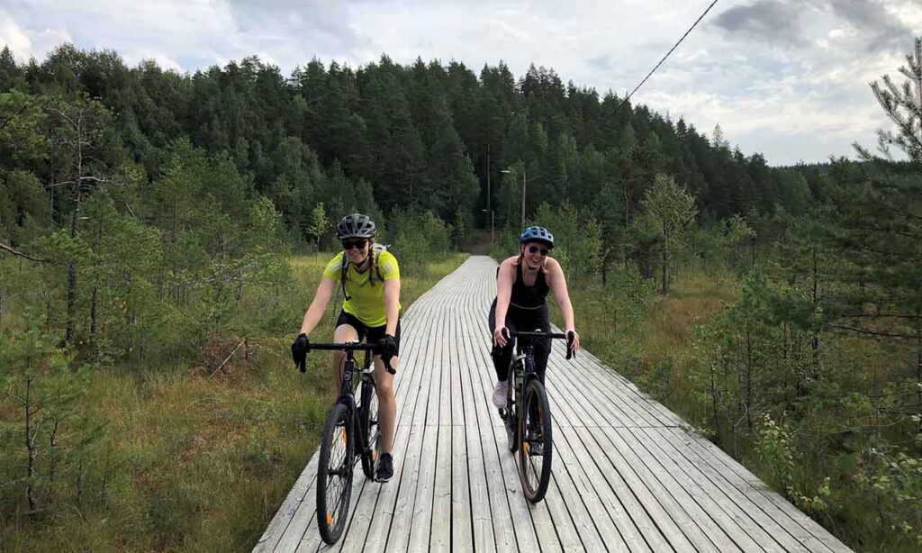 [Alt-teksti: Kaksi pyöräilijää polkemassa metsäisessä maisemassa laudoitetun pyörätien päällä.]