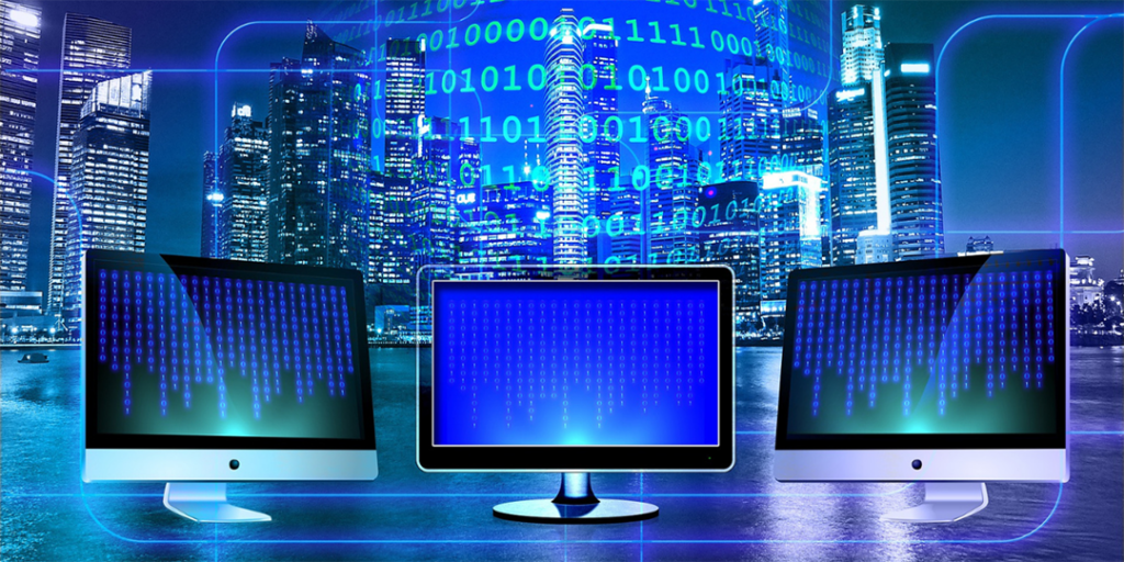 Sinisävyinen kuva jossa kolme tietokonenäyttöjä ja binäärijärjestelmä. Taustalla pilvenpiirtäjiä