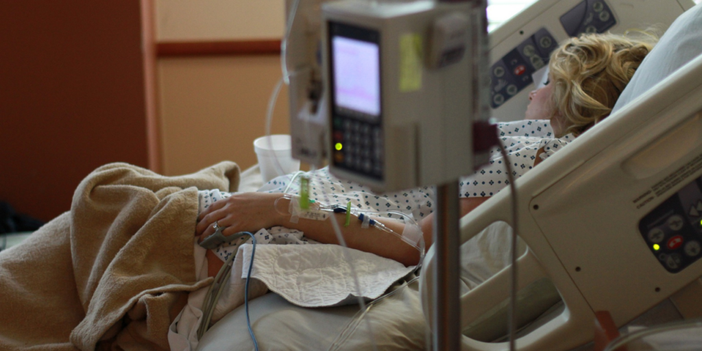 Ihminen makaa sairaalasängyssä ja häneen on kytketty erilaisia laitteita, jotka mittaavat häneen tilaansa