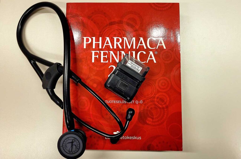 (ALT-teksti: Kuvassa on Pharmaca Fennica -lääkeopas, leimasin ja stetoskooppi)