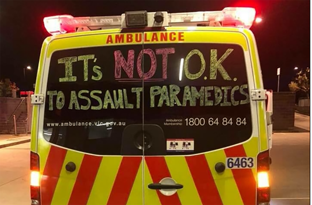 [Alt-teksti: ambulanssin perä. Takaikkunaan on liituväreillä kirjoitettu suurin kirjaimin it's not o.k. to assault paramedics.]