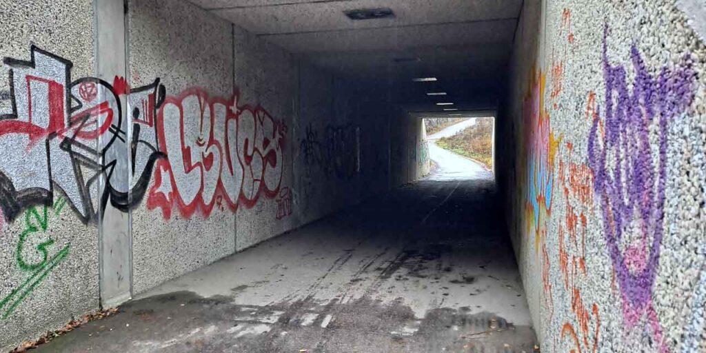 Alt-teksti: Kuvassa on kevyelle liikenteelle tarkoitettu alikulkutunneli, joka on kapea ja pimeä ja jonka seinissä on graffiteja.