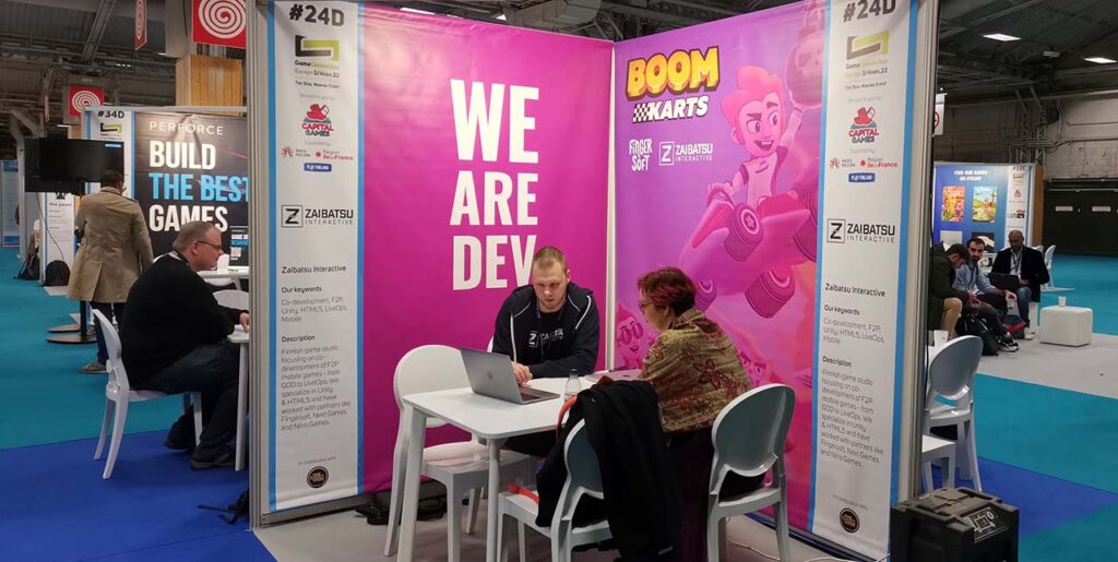Two people inside pink booth with text We Are Dev. In the background more similar small booths and people
