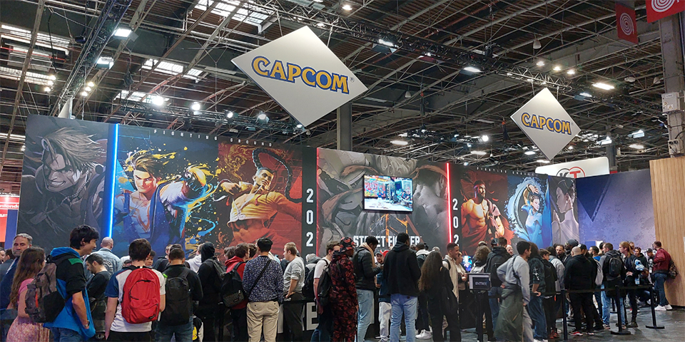 Capcom näytteilleasettajan messupiste, jossa ihmiset jonottavat. Messupisteen seiniä koristavat yrityksen logot sekä kuvat Street Fighter pelistä. 