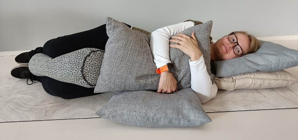 [Alt-teksti: nainen makaa kyljellään tyynyjen ympäröimänä ja tyynyjä halaillen.]