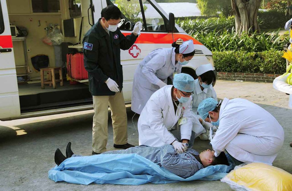 [Alt-teksti: onnettomuustilanne. Mies makaa maassa ambulanssin vieressä ja hänen ympärillään on ryhmä ensihoitajia auttamassa.]