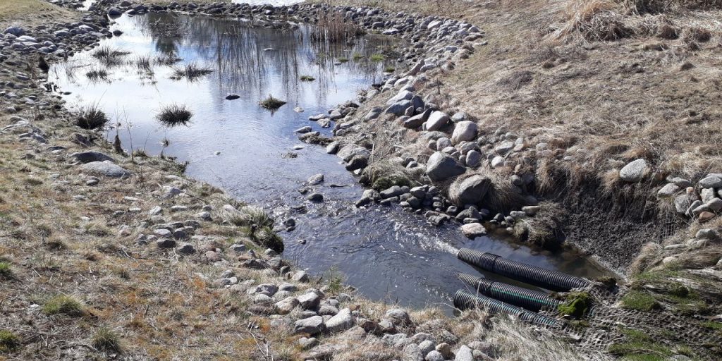 Three pipes from underground leading water to a rocky stormwater basins.