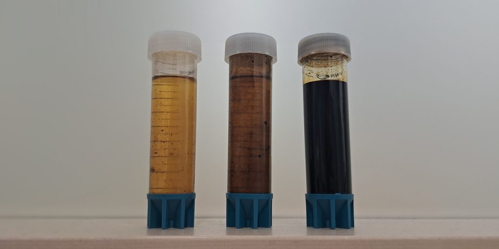 Kolme läpinäkyvää n. 15 cm pitkää muoviputkea rivissä, ja niiden sisällä keskenään eri näköisiä pyrolyysiöljyjä. Vasemmanpuoleisessa on kirkasta kellertävää nestettä, keskimmäisessä vähän tummempaa ja viimeisessä läpinäkymätöntä mustaa öljyä.