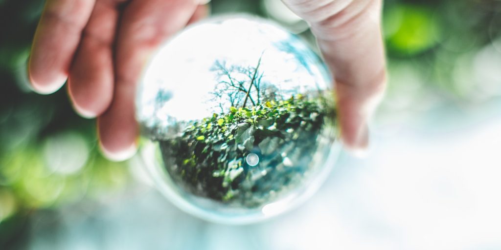 In the centre, there is a glass lensball and a hand holding it. The lensball reflects the nature background.