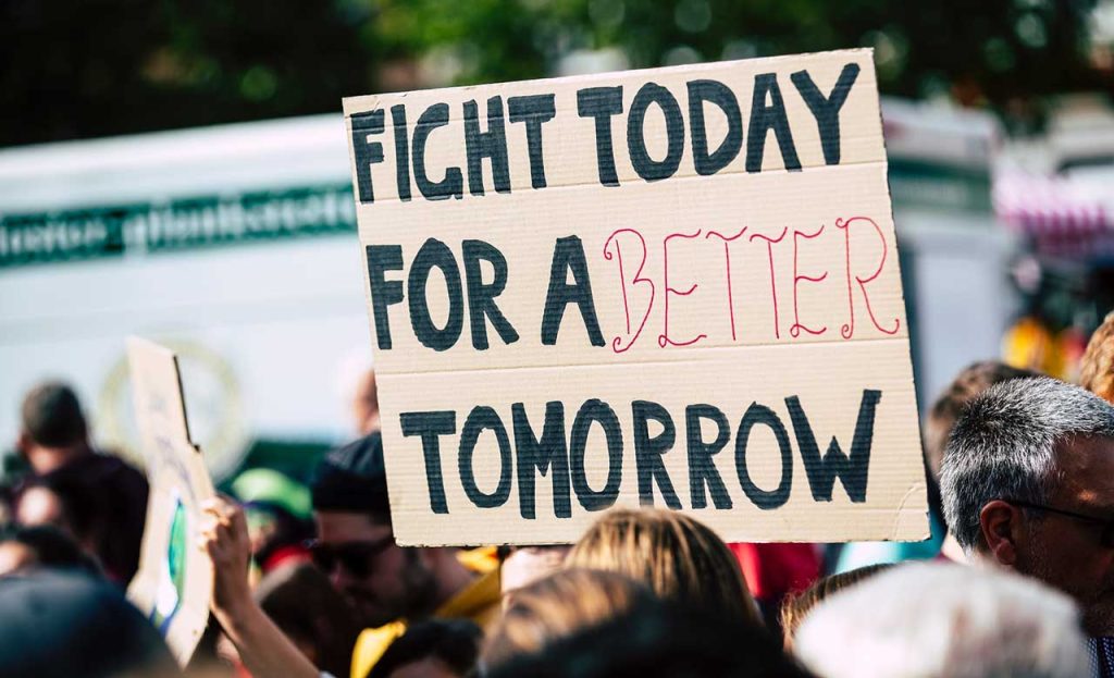 [alt-teksti Ihminen pitelemässä kylttiä, jossa lukee: ”Fight today fo a better tomorrow”]
