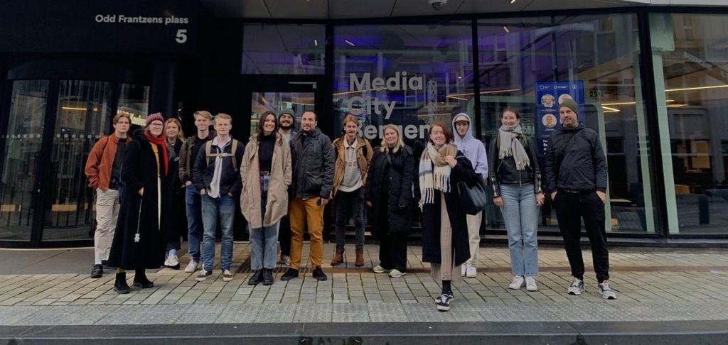 [Alt-teksti: ryhmä ihmisiä seisomassa kadulla suurten lasiovien edessä, ovissa lukee Media City Bergen.]