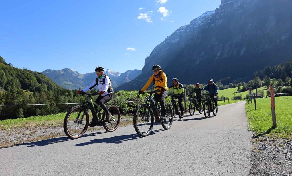 [Alt-teksti: joukko pyöräilijöitä jylhien vuorten viertä kulkevalla  pyörätiellä.]