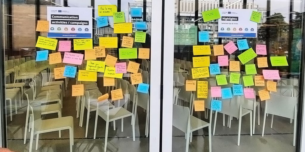 A glass wall on which there are colourful post-it notes with tips on communication activities/ campaigns on the left, and on highlights on the right.