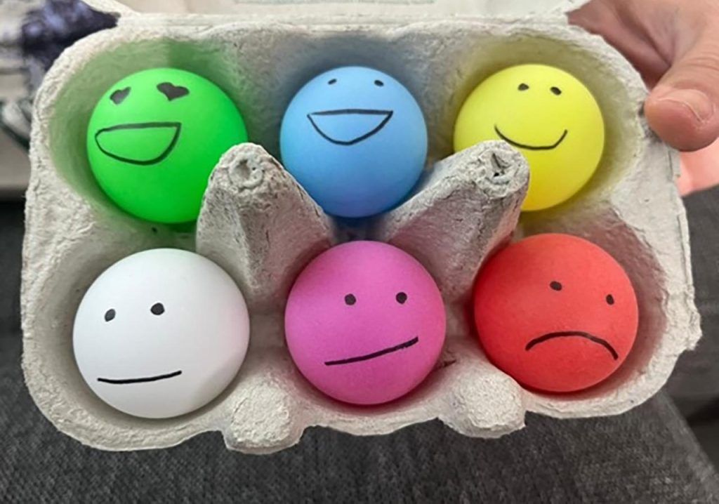 [Alt-teksti: munakennossa on kuusi eriväristä palloa, joille on piirretty tunteita ilmaisevat naamat.]