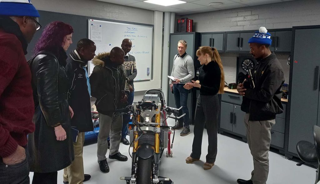 [Alt text: a group looking at electric motor cycle in a laboratory environment.]