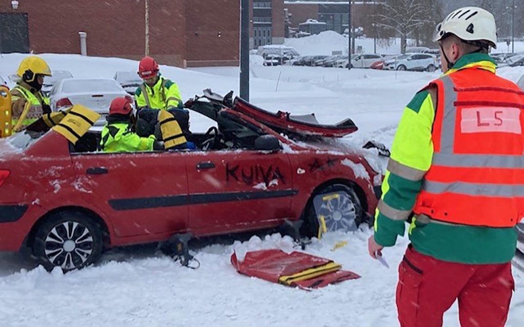 [Alt-teksti: onnettomuuden harjoittelutilanne talvisella pihalla, autonromun ympärillä on pelastusasuisia henkilöitä.]