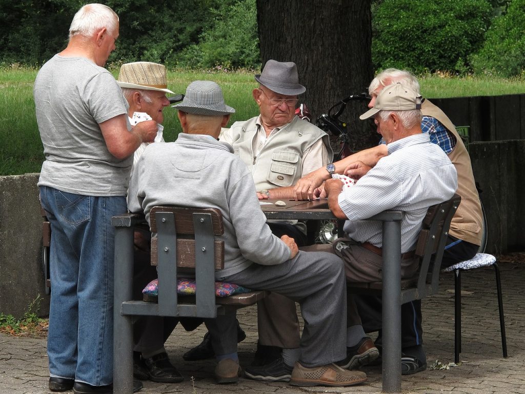 Ryhmä vanhoja miehiä puistossa pelaamassa korttia.