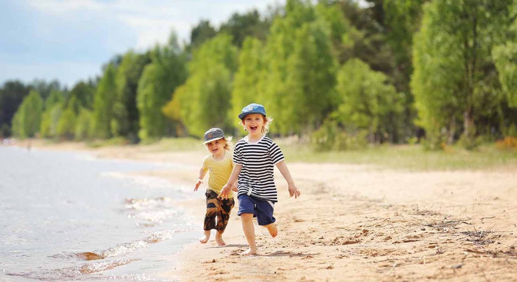 [Alt-teksti: kaksi pientä lasta juoksemassa hiekkarannalla aurinkoisena päivänä.]