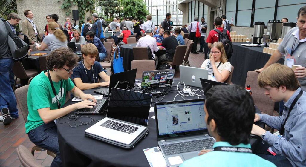 [Alt text: dozens of people working with their laptops in a big hall.]