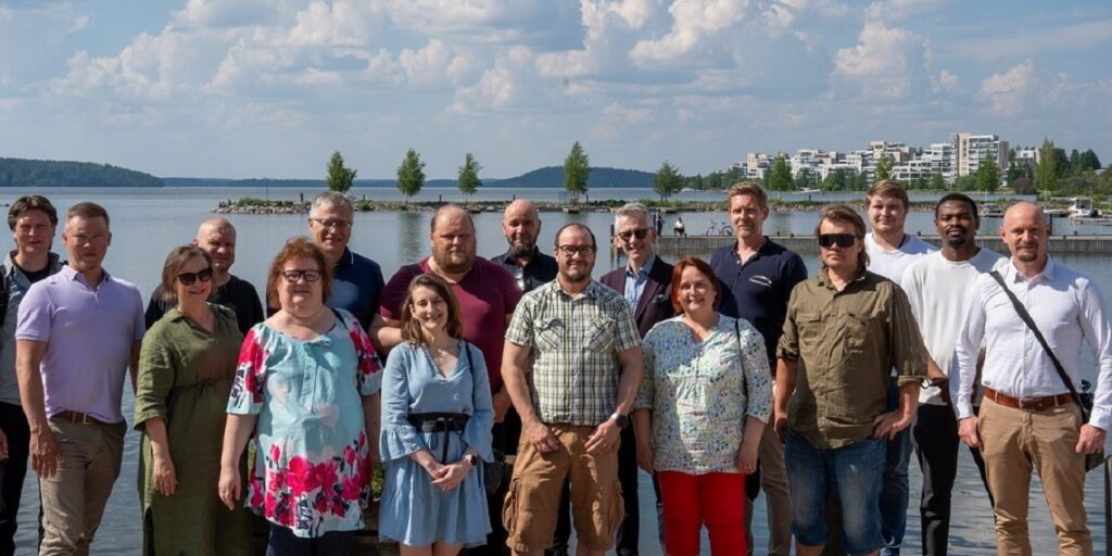 17 henkilöä Lahden Sibeliustalon vieressä, taustalla Vesijärvi. He osallistuivat workshop-tilaisuuteen. 