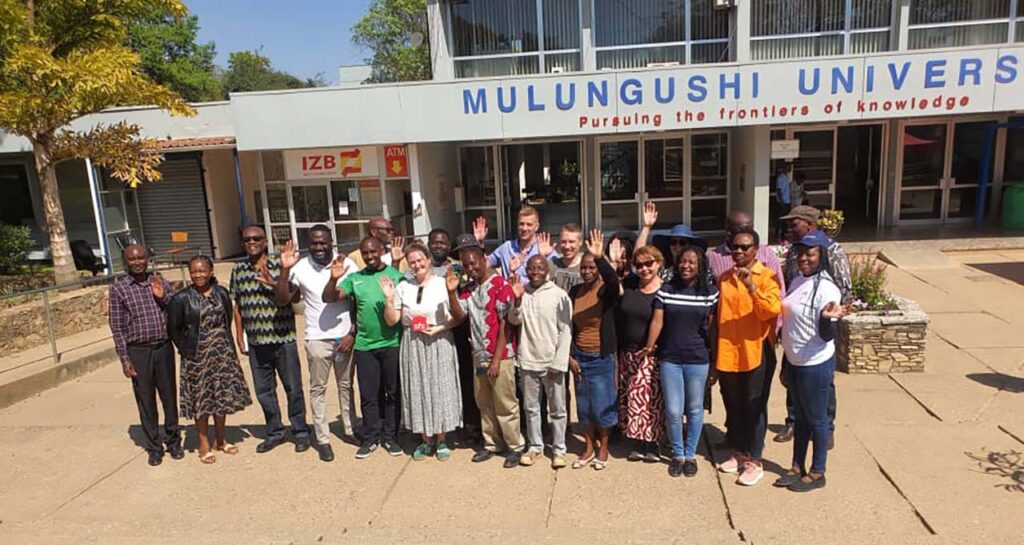 [Alt text: large group of smiling people standing in front of Mulungushi University building.]