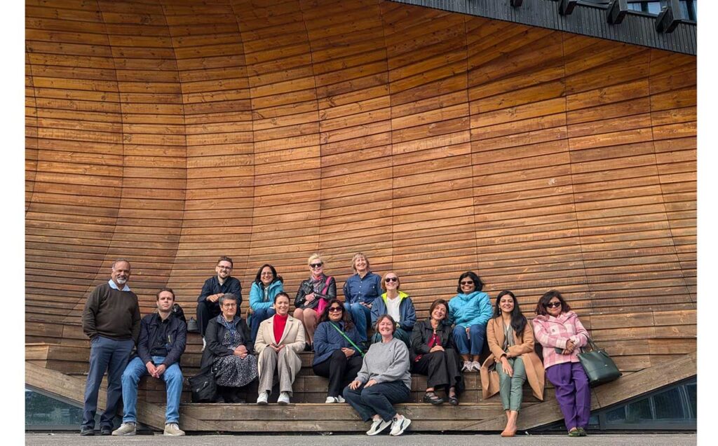 [Alt text: a group of persons in front of a massive, high wooden panel wall.]