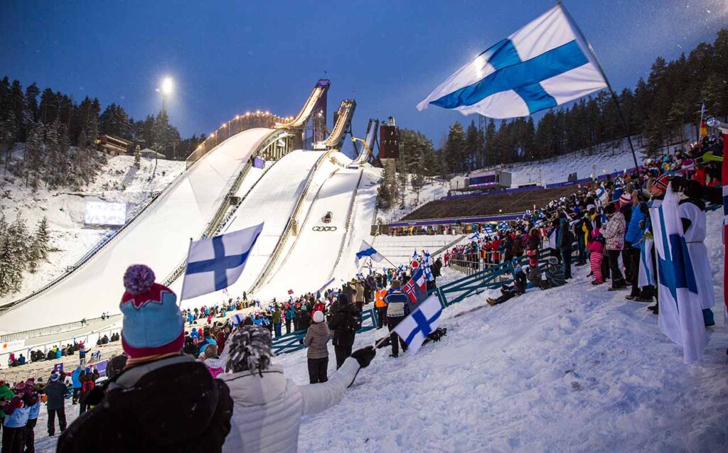 [Alt text: Lahti's famous ski-jumping hills at night with audience and flags.]