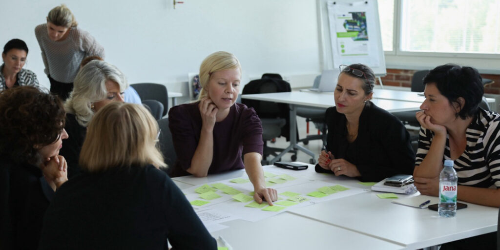 A group of people discussing around a table at the DeCo Interregional Event.