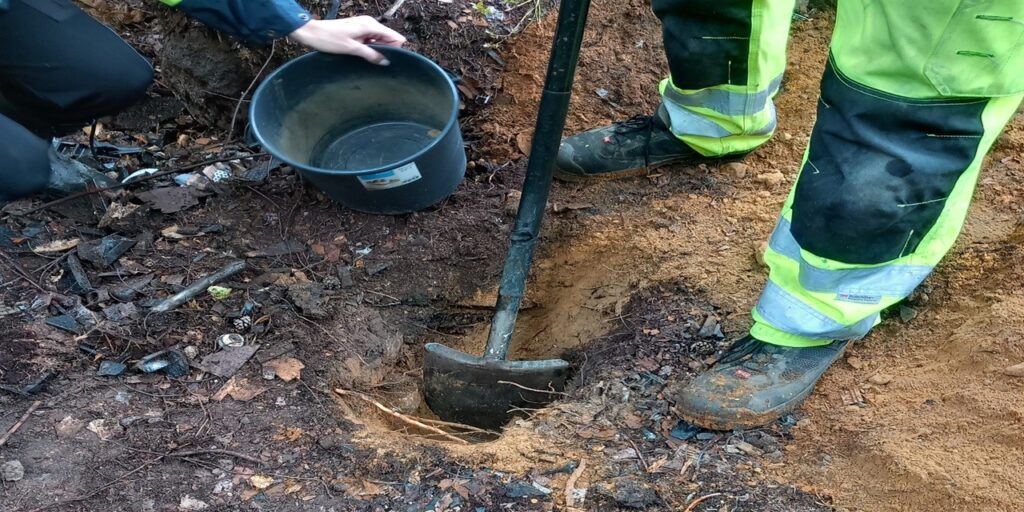 Huomiovaatteisiin pukeutunut henkilö kaivaa lapiolla kuoppaa maahan.