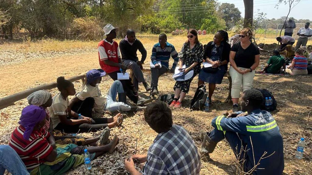 [Alt text: a group of people sitting and discussing outdoors.]