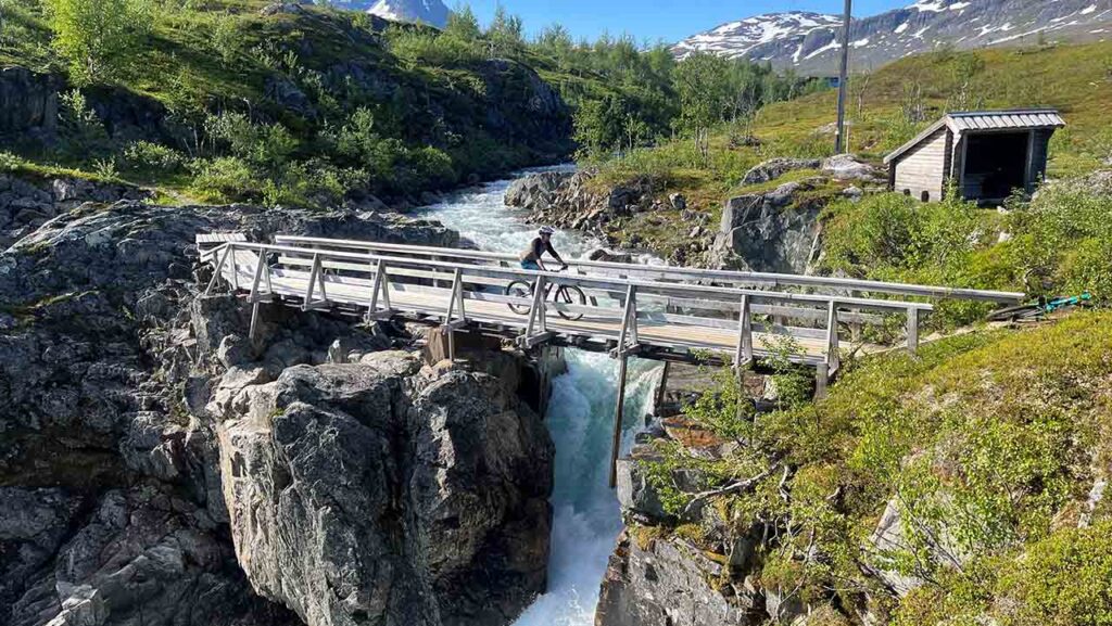 [Alt-teksti: jylhä maisema, koski juoksee kallioiden välissä, pyörätie vie kosken yli.]