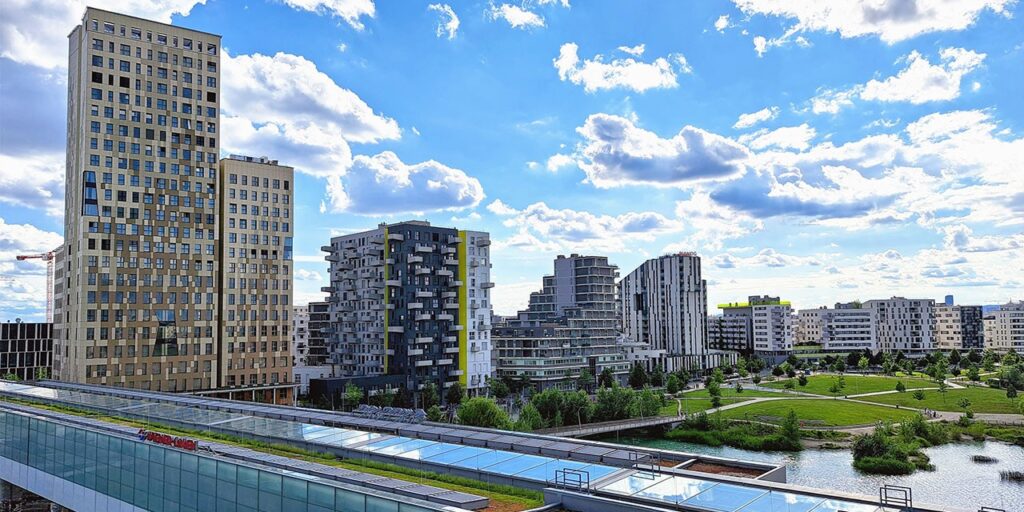 A photo from outdoor with several modern buildings. The building on the left is the tallest from all.