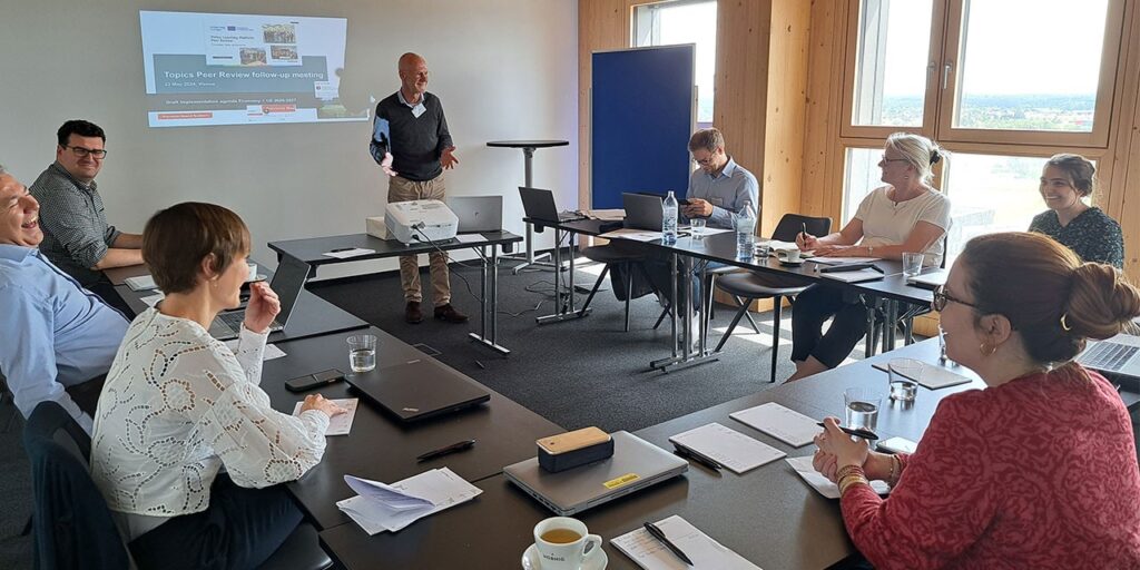 People sitting around an U-shaped table. In the middle there's a person giving a presentation.