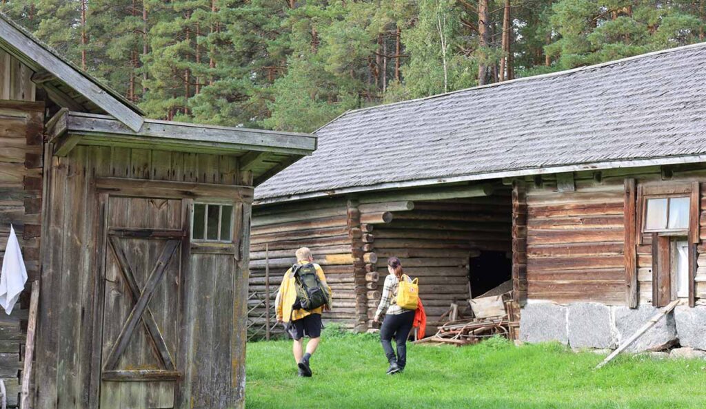 [Alt-teksti: kaksi henkilöä perinnepihassa matkarinkat selässään.]