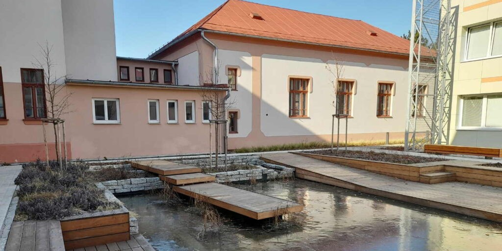 An example of water retention measures. A frozen body of water surrounded by wooden platform structures, plantings, and buildings.