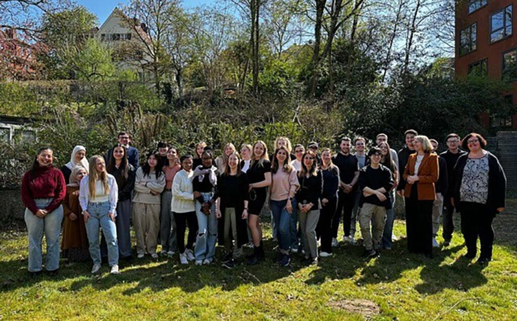 [Alt text: a large group of people standing outside in sunshine.]