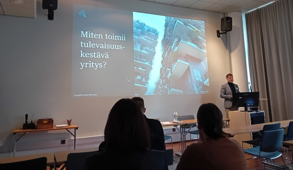[Alt-teksti: henkilö pitämässä esitystä luentosalissa, näyttöseinällä lukee miten toimii tulevaisuuskestävä yritys.]