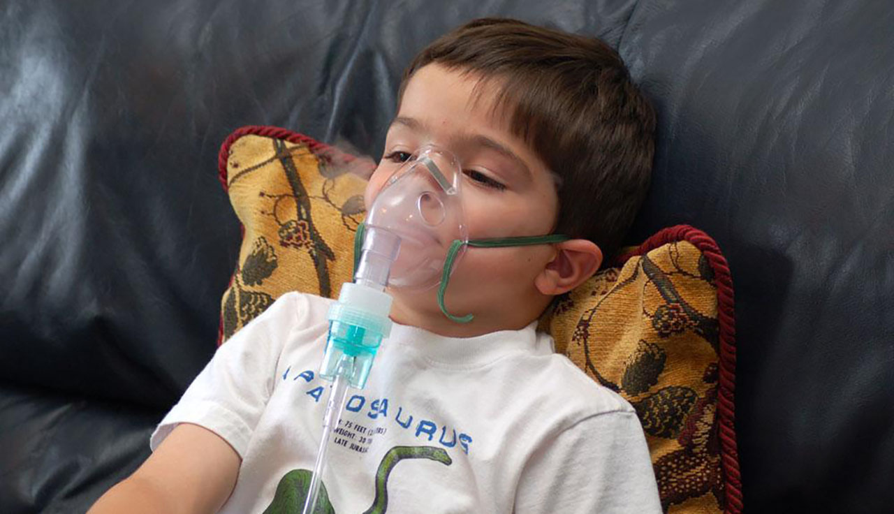 [Alt-text: A small boy is lying on a pillow with an oxygen mask on his face.]